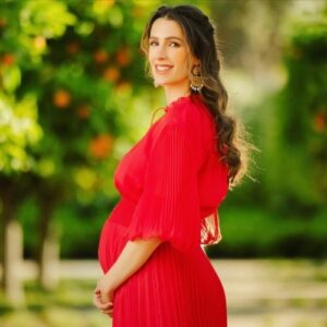 الأميرة رجوة الحسين بفستان أحمر بكسرات (Pleated) مكشوف الكتفين، مع تسريحة شعر مموجة ناعمة ومكياج طبيعي يبرز ملامحها الهادئة.