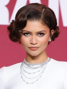 الكلاسيكية الهوليودية (صورة 1): استوحت إطلالتها من العصر الذهبي للسينما، مع غرة جانبية "Finger Waves" مصقولة بعناية وخصلات ملفوفة للخلف، مما أعطاها مظهراً ملكياً يتناسب مع المجوهرات الماسية الفاخرة.